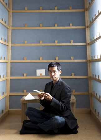 Colour photograph of Lee Mingwei sitting reading a letter in the Letter Writing booth