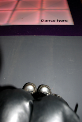 Colour photograph showing my knees and feet (in boots) going up the ramp to a coloured floor with a sign saying 'dance here'