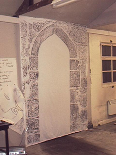 shows stone rubbing of an archway hanging on the wall in Rita's hut