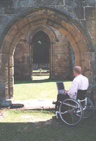 shows a man using a wheelchair and laptop by an arch