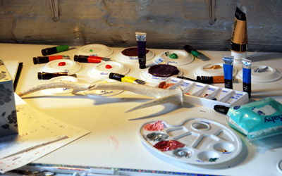 Colour photograph showing the antler on a drawing board, surrounded by tubes of paint and palettes.