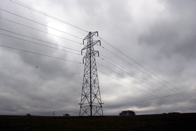 Colour photograph of an electricity pylon outlined against a stormy grey sky