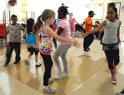 Colour photograph of young children enthusiastically dancing in a community centre.