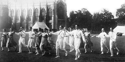 Black and white photograph of two rows of dancers coming forward with linked hands outside Cheltenham Cathedral
