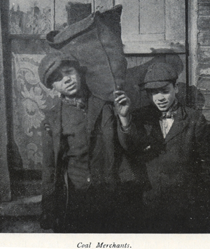 Black and white photograph showing two young boys carrying sacks of coal.