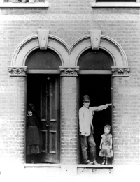 Black and white photograph of a man and a small girl standing in the doorway of a terraced house