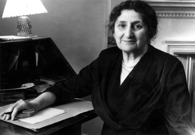 Black and white photograph of an older Maud Karpeles smiling at the camera as she sits at her desk