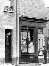 Black and white photograph of a man standing outside of a shop
