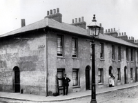 Black and white photograph of a man outside a street of terraced houses