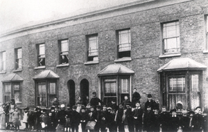 Black and white photograph of children posing for the photographer outside their houses