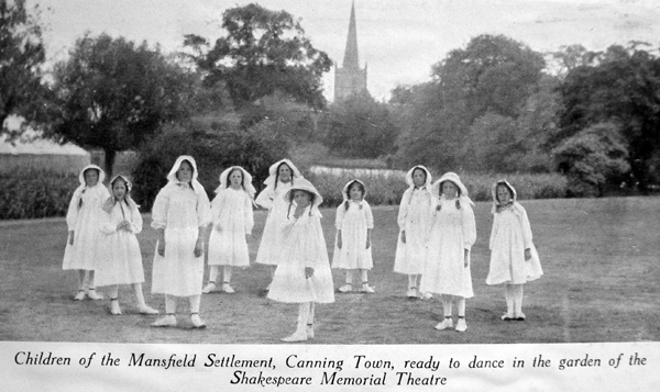 Black and white photograph of ten girls dressed in white smocks and caps, standing in a circle.
