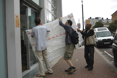 Colour photograph of three men carrying a giant wrapped package into a building