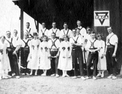 Black and white photograph of men and women in folk dance clothing outside a building with a YMCA sign