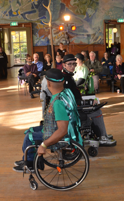 Close-up of wheelchair users dancing in a hall.