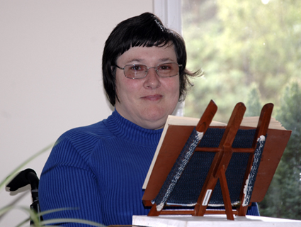 Colour photograph of Helen Aveling, smiling over the top of a book