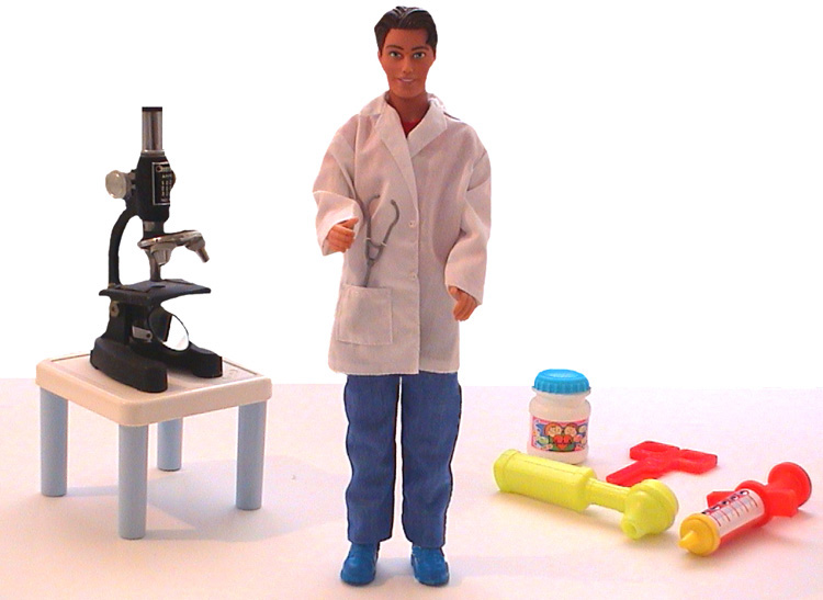 A male doll dressed as a doctor faces front against a white background. Behind him are a child's medical kit and microscope.
