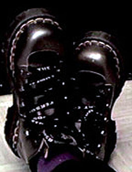 Photograph of a woman's feet in silver and black boots, crossed at the ankles as she lies on the floor.