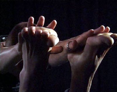 Colour photograph of a woman resting her hands on another woman's upturned feet, as they balance together.