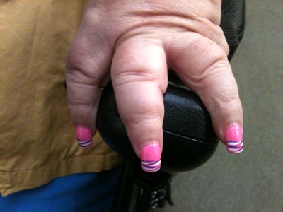 Colour photograph of three fingers with brightly decorated pink nails, resting on the control of a wheelchair.