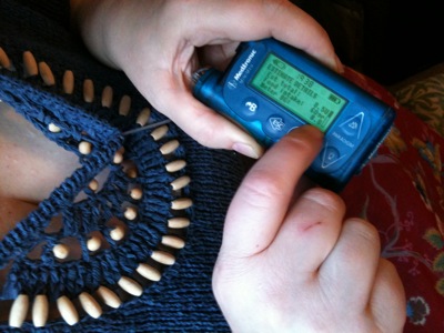 Colour photograph of a woman's hands holding and entering information into a blue digital monitor attached to a tube which disappears into her beaded blue top.