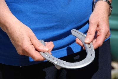 Colour photograph of a woman's hands holding a silver horseshoe against a background of a royal blue polo shirt.