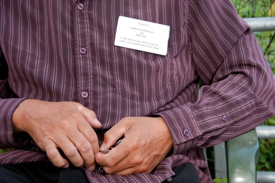 Colour photograph of a man's tanned hands against a background of a striped maroon shirt.