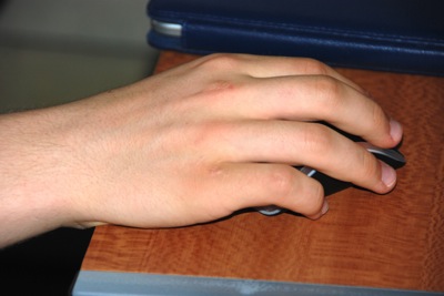 Colour photograph of a teenager's hand resting on a computer mouse against a wooden desk.