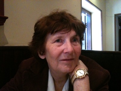 Colour photograph of an older white woman, with shortish brown hair and a prominent gold-coloured watch on her wrist.