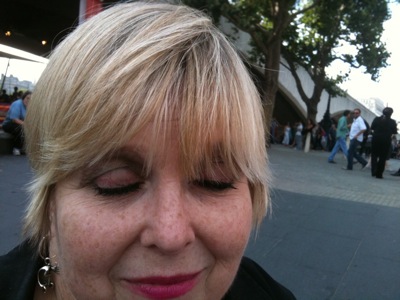 Colour photograph of a woman with bobbed blonde hair looking down to show off her painted eyelids.
