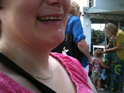 Close up colour photograph of a pale-skinned woman wearing a pink top and laughing.