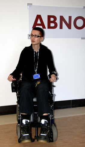 Colour photograph of the artist sitting in a power wheelchair, in front of a sign saying Abnormal