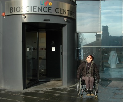 Colour photograph of the artist sitting in her chair outside of the Bioscience Centre in Newcastle
