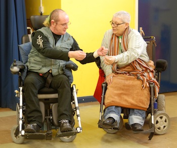Colour photograph of two wheelchair users, a man and a woman, improvising a scene